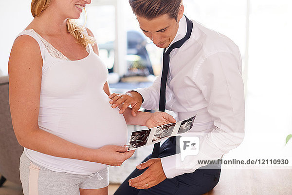 Schwangeres Paar betrachtet Ultraschallbilder im Wohnzimmer