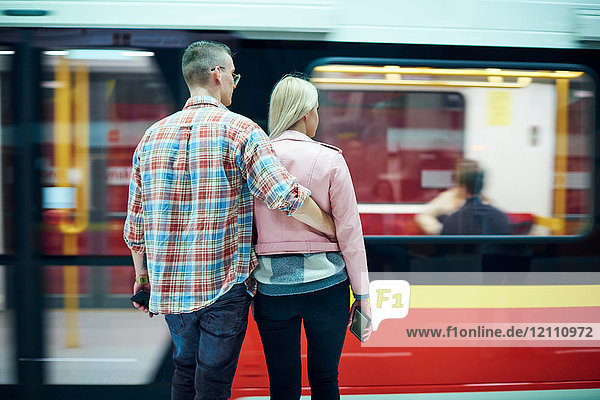 Rückansicht eines jungen Paares  das an der städtischen Straßenbahnhaltestelle wartet