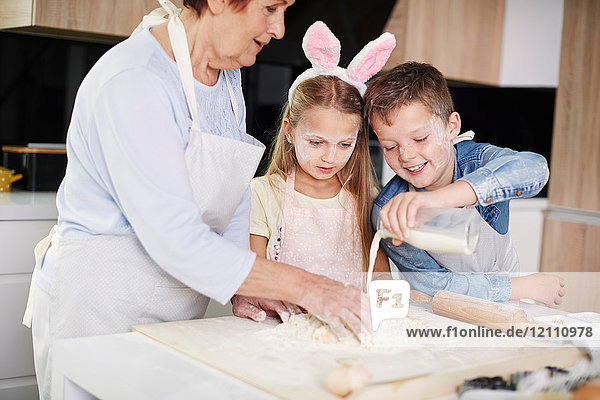 Mädchen und Bruder helfen Großmutter beim Osterbacken an der Küchentheke