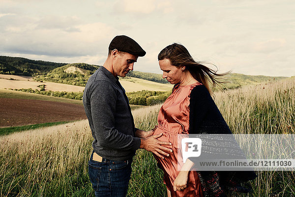 Romantic man with hands on pregnant wife's stomach on hillside