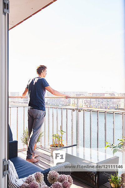 Mittelgroßer erwachsener Mann  der vom Balkon des Apartments am Wasser hinaussieht