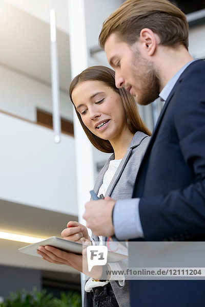 Junge Geschäftsfrau und Mann benutzen digitales Tablet im Büro-Atrium