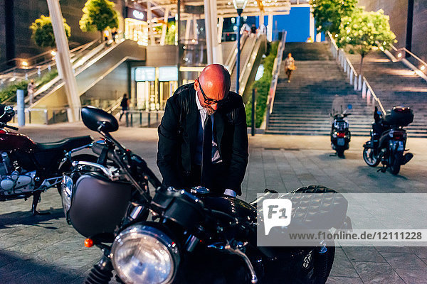 Ein reifer Geschäftsmann  der sich nachts im Freien auf das Motorradfahren vorbereitet