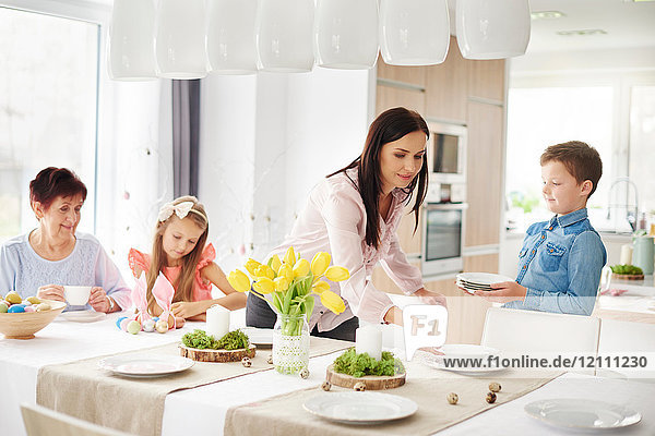 Frau und Familie bereiten Tischgedecke am Ostertisch vor