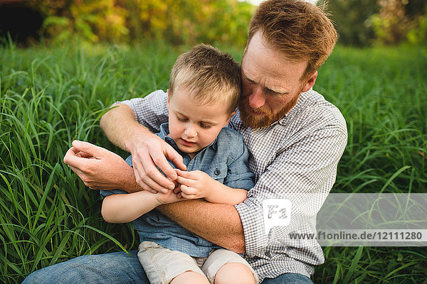 Vater und Sohn sitzen im hohen Gras und erforschen die Natur
