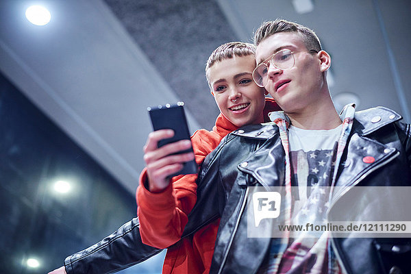 Junges Paar bewegt sich auf der Rolltreppe einer U-Bahn-Station nach unten und schaut auf ein Smartphone