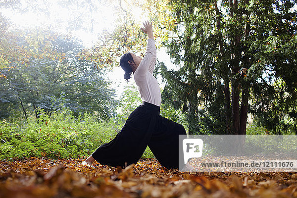 Volle Länge der Frau  die Yoga macht  während sie im Herbst an Bäumen im Park steht.