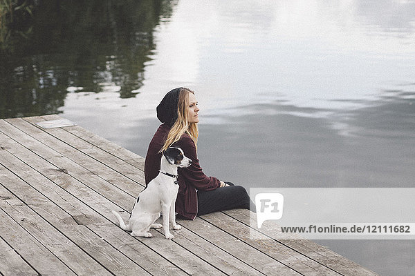 Nachdenkliche Frau sitzend mit Hund am Steg über dem See