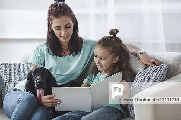 Mädchen-Lesebuch von Mutter und Hund auf dem Sofa zu Hause