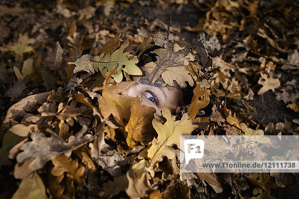 Nahaufnahme einer Frau  die im Herbst mit trockenen Blättern bedeckt ist.