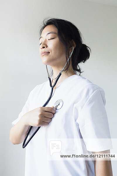 Female doctor listening self heart beat with stethoscope against wall