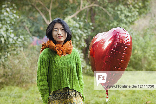 Porträt einer Frau in Form eines roten Herzballons im Park
