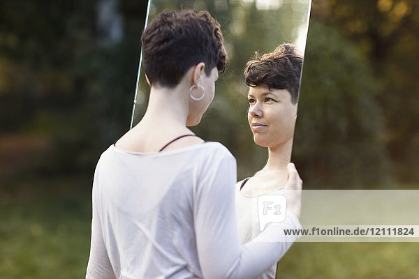 Smiling woman with short hair looking in mirror while standing at park