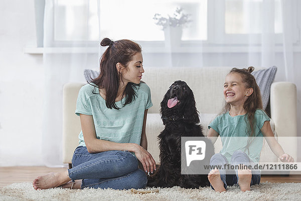Fröhliches Mädchen sitzend bei Cocker Spaniel und Mutter im Wohnzimmer zu Hause