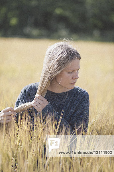 Nachdenkliche Frau mit langen Haaren inmitten von Gras bei Sonnenschein