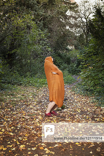 Volle Länge der Frau mit orangem Schal bedeckt  die im Herbst im Park tanzt.