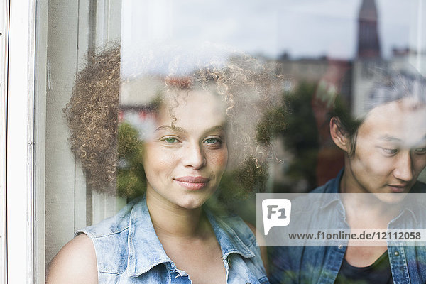 Porträt einer lächelnden Frau stehend mit Mann durch ein Glasfenster gesehen
