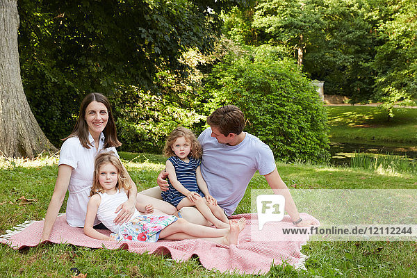 Porträt mittelgroßer Eltern und zwei Töchter auf Picknickdecke im Park