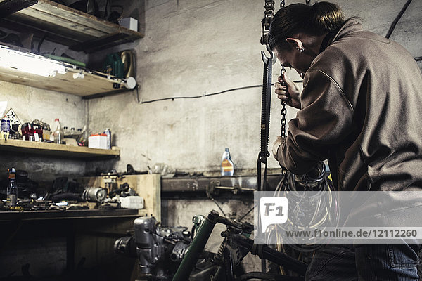 Mechanic hoisting dismantled vintage motorcycle in workshop