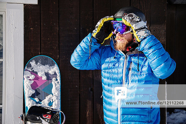 Man in skiwear  adjusting goggles  snowboard beside him