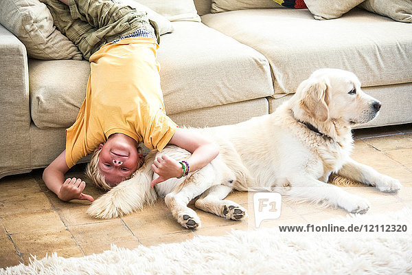 Junge kopfüber auf dem Sofa liegend mit Hund