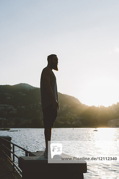 Hinterleuchteter junger männlicher Hipster  der vom Wasser aus auf den Comer See schaut  Comer See  Lombardei  Italien