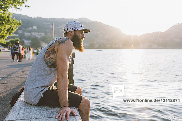 Junger männlicher Hipster sitzt auf einer Mauer und schaut auf den Comer See  Lombardei  Italien