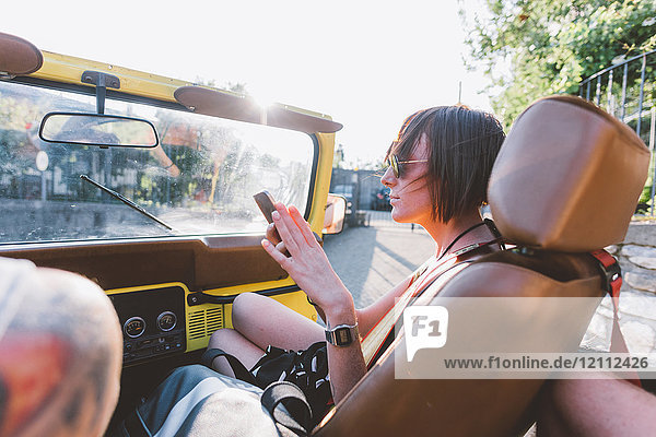 Young woman looking at smartphone in off road vehicle  Como  Lombardy  Italy
