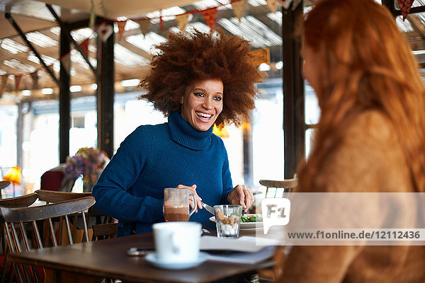 Frau isst mit Freundin im Cafe und lächelt