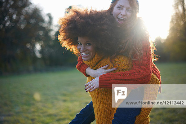 Zwei junge Frauen in ländlicher Umgebung  junge Frau nimmt ihren Freund Huckepack
