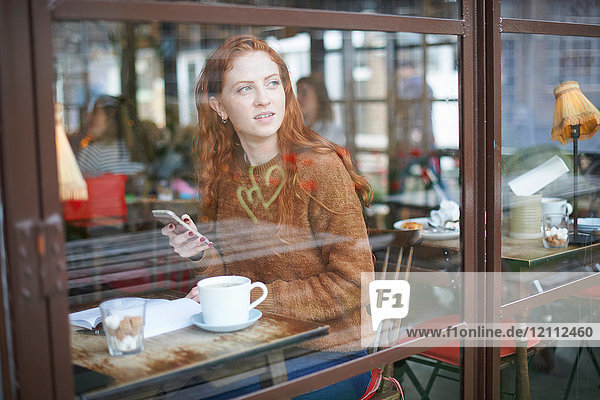 Blick durch das Fenster einer Frau im Café mit einem Mobiltelefon