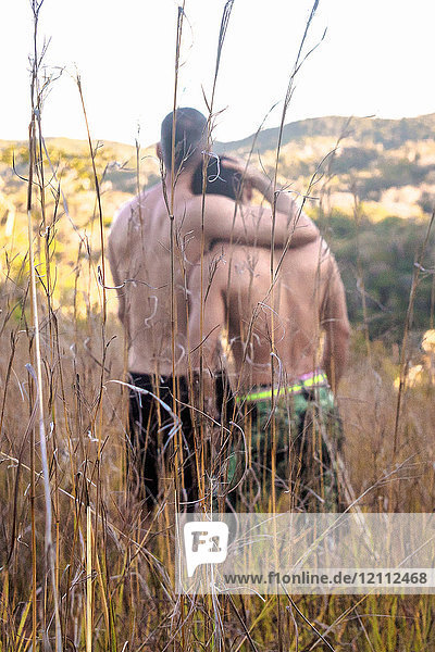 Rear view of two bare chested men looking out at landscape from long grass  Guaramiranga  Ceara  Brazil