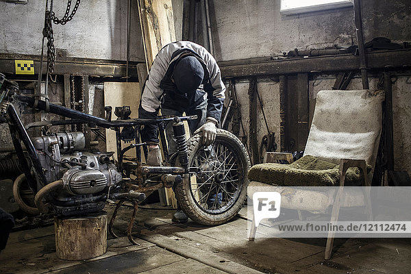 Mechanic adjusting wheel on dismantled vintage motorcycle in workshop