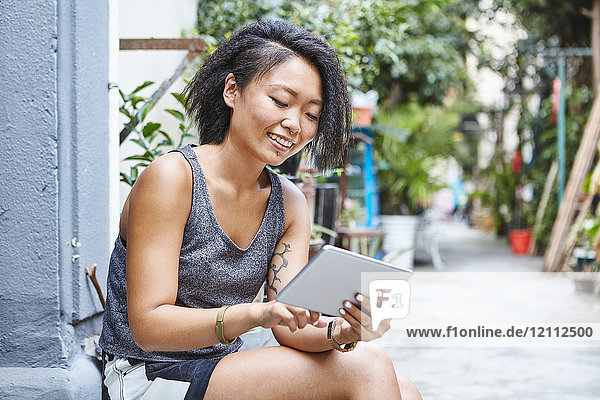 Frau sitzt auf der Türschwelle in einer Wohngasse und schaut auf ein digitales Tablet  Shanghai French Concession  Shanghai  China