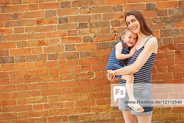 Portrait of pregnant mid adult woman carrying daughter by brick wall