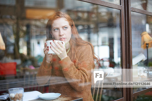 Blick durch das Fenster einer Frau im Kaffeehaus  die eine Tasse hält