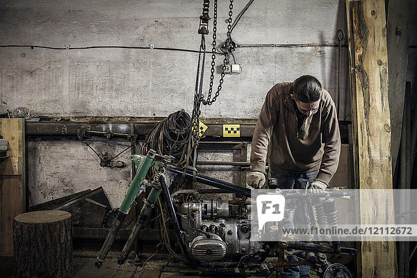 Mechanic inspecting dismantled vintage motorcycle in workshop