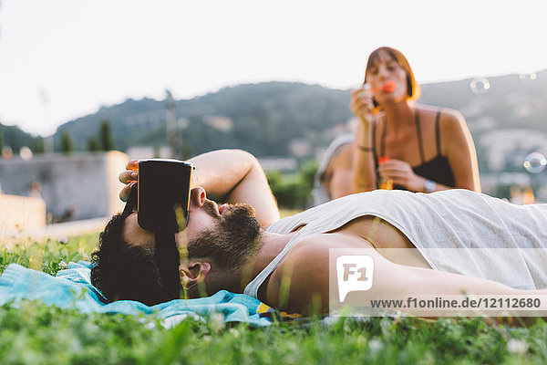 Junger Mann liegt im Gras und schaut durch ein Virtual-Reality-Headset  Como  Lombardei  Italien