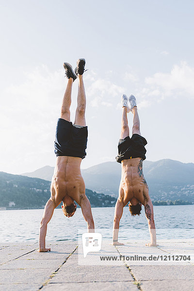 Zwei junge Männer machen Handstand am Wasser  Comer See  Lombardei  Italien