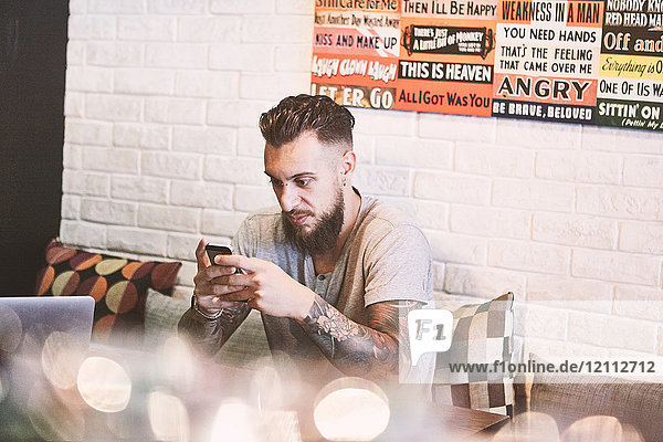 Junger männlicher Hipster im Café mit Blick auf Smartphone  Shanghai French Concession  Shanghai  China