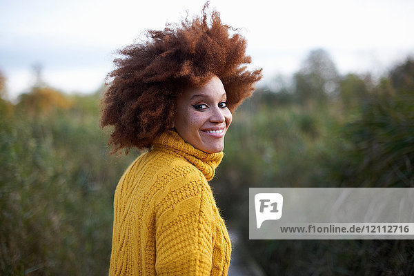 Porträt einer Frau mit Afro  die über die Schulter schaut und lächelnd in die Kamera blickt