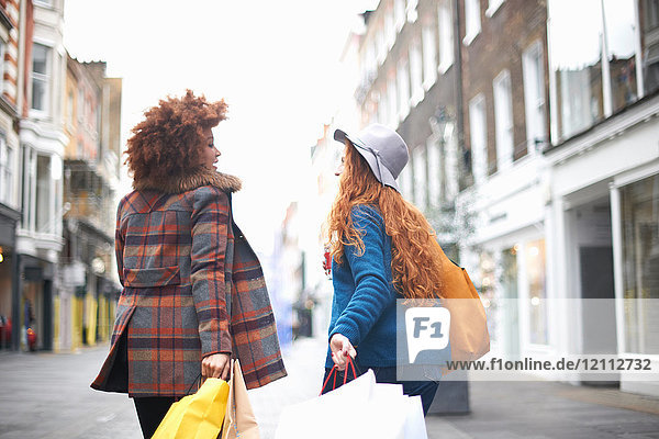 Two young women  walking along street  holding shopping bags  rear view
