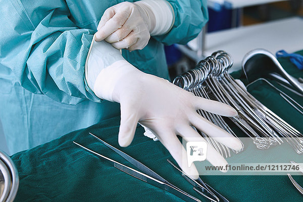 Chirurg zieht Operationshandschuhe im Operationssaal der Entbindungsstation an