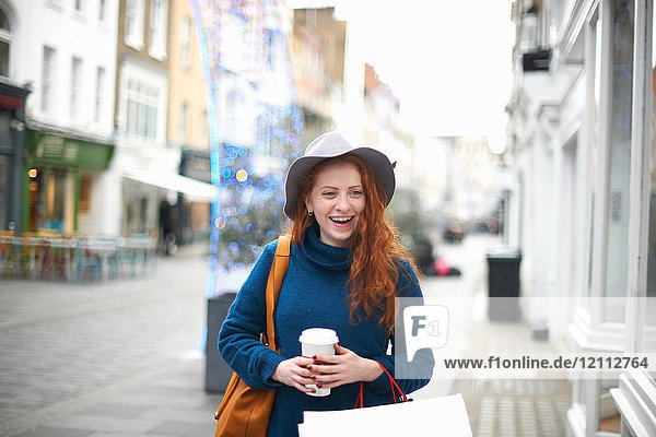 Junge Frau geht auf der Straße  hält Kaffeetasse und Einkaufstasche
