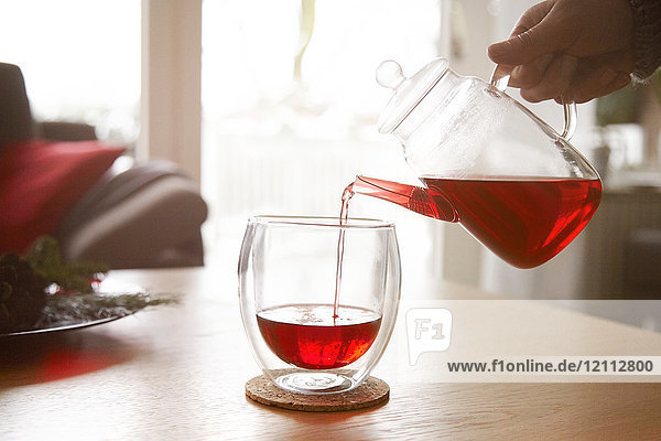 Frau gießt roten Tee in Glas