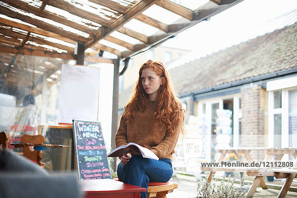 Woman at coffee shop holding notebook looking solemn