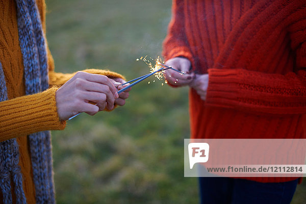 Two young women  in rural setting  lighting sparklers  mid section