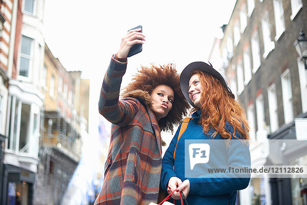 Two young women in street  taking selfie  using smartphone  low angle view