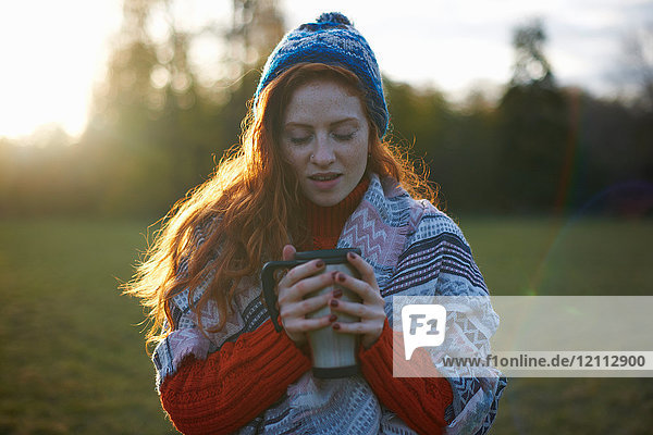 Junge Frau in ländlicher Umgebung  in eine Decke gewickelt  in der Hand ein heißes Getränk