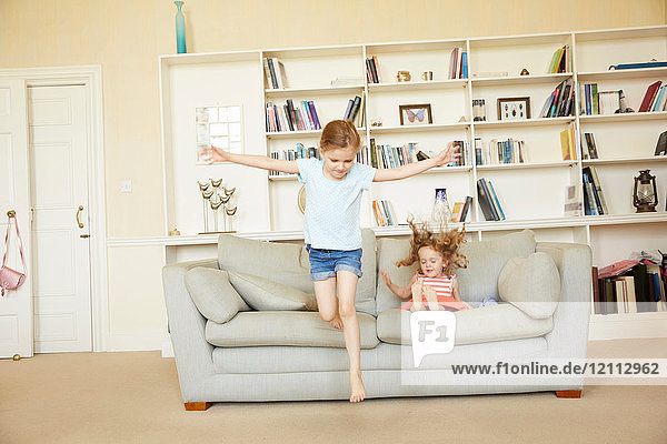 Two young sisters jumping from and bouncing on sofa